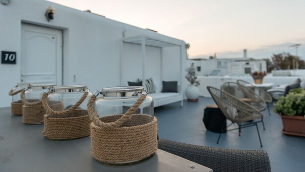 A rooftop terrace with wicker baskets on tables, white furniture, and a building with a number '10' sign. - Orpheas Rooms (Mykonos)