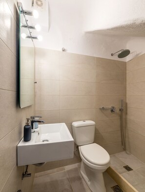 A modern bathroom with a white sink, toilet, and shower. - Orpheas Rooms (Mykonos)
