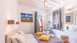A modern bedroom with two beds, a bathroom, and a view of a red building. - Orpheas Rooms (Mykonos)