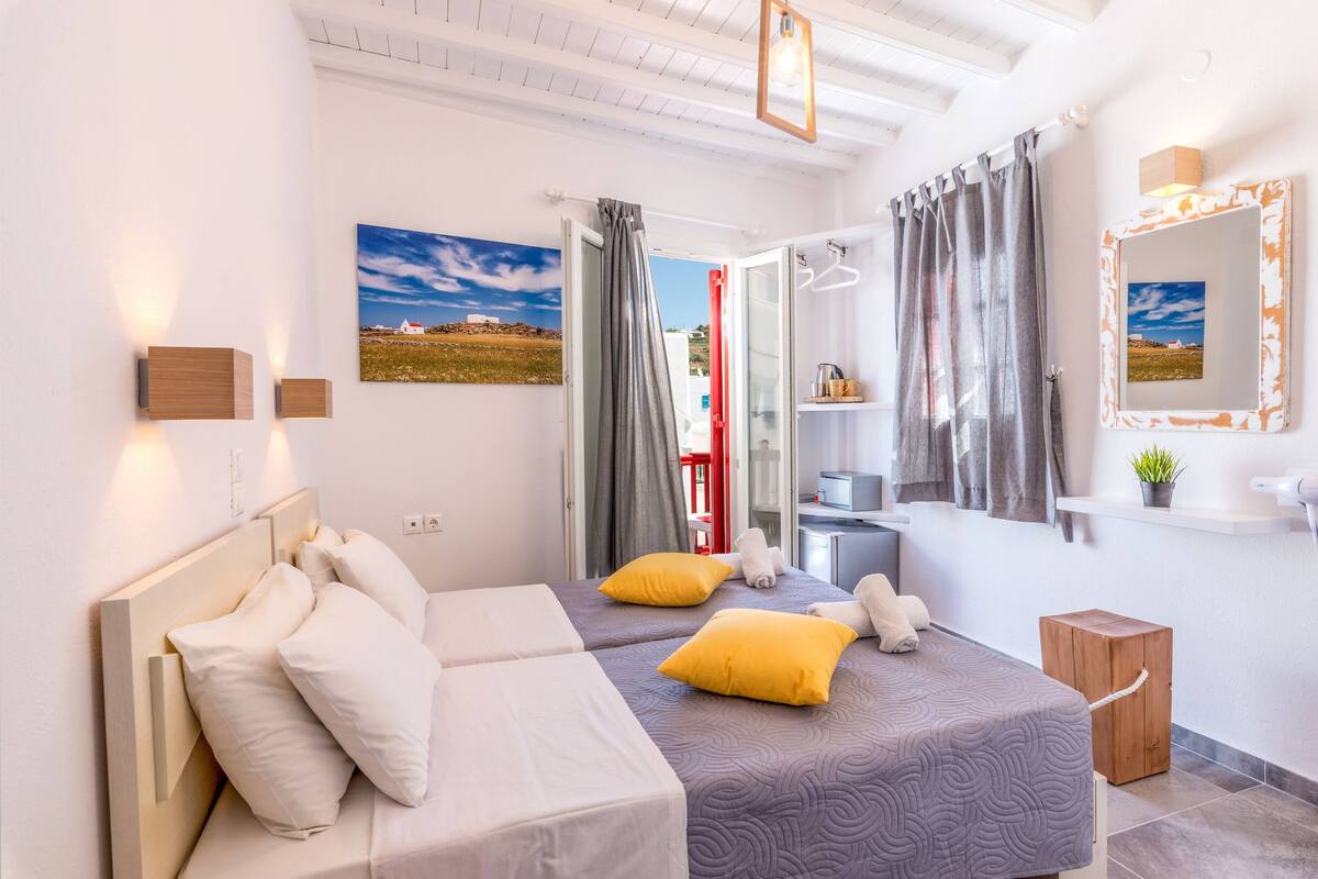 A modern bedroom with two beds, a bathroom, and a view of a red building.
