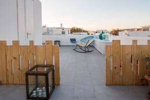 A rooftop terrace with a wooden fence, a glass table with candles, a laptop, and a blue chair. - Orpheas Rooms (Mykonos)