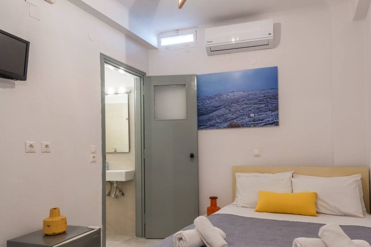 A modern hotel room with a bed, a TV, an air conditioning unit, and a painting on the wall.