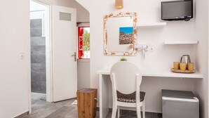 A compact room with a white desk, a chair, a TV mounted on the wall, and a small trash bin. - Orpheas Rooms (Mykonos)
