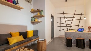 A modern living room with a grey sofa, wooden side tables, and a desk with a laptop. - Orpheas Rooms (Mykonos)