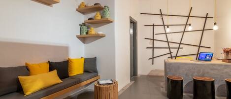 Una sala de estar moderna con un sofá gris, mesitas de madera y un escritorio con una computadora portátil.