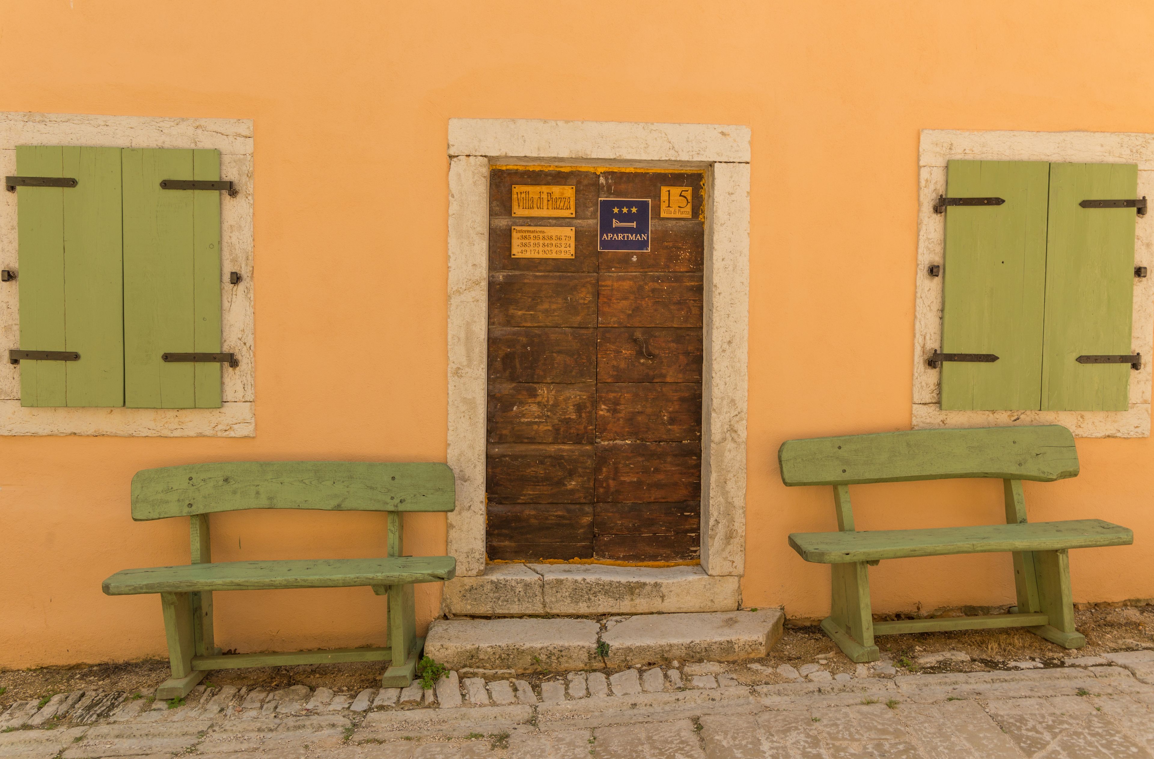 A building with a wooden door and two green benches in front.