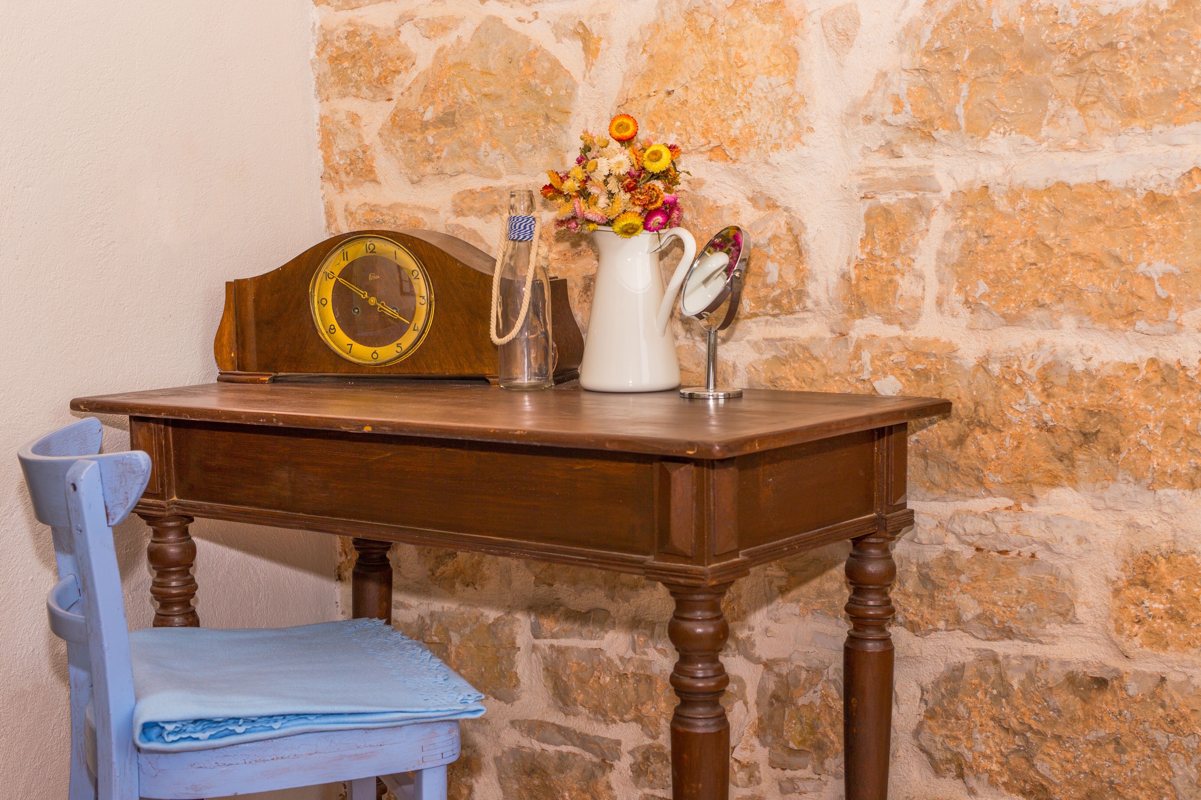 Une table en bois, une horloge, un vase avec des fleurs et un miroir.