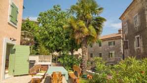 Un patio con una mesa y sillas, un banco, una palmera y un muro de piedra.