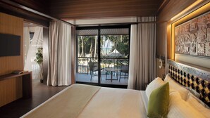 Ein Hotelzimmer mit einem großen Bett, einem Fernseher, einem Balkon mit Sitzgelegenheit und Blick auf Palmen.