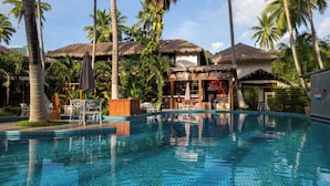 Ein Schwimmbecken mit Bar, Palmen und strohgedeckten Hütten.