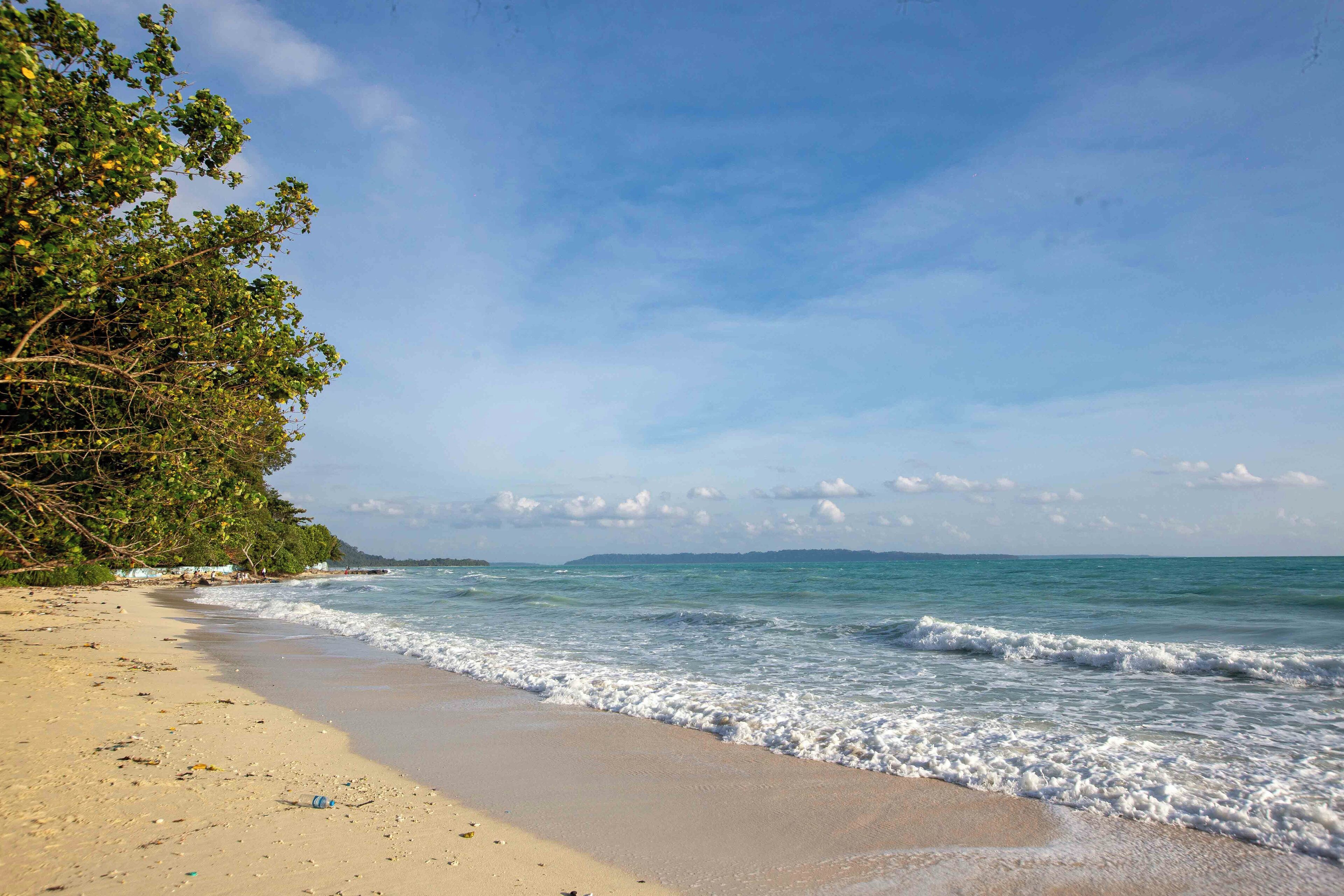 A beach with clear skies, gentle waves, and a sandy shore.