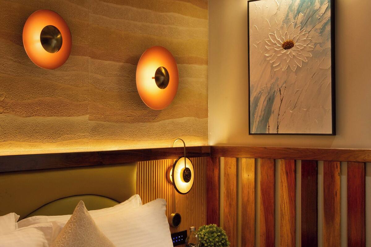 A modern hotel room with a wooden ceiling, a large bed with white linens, two wall-mounted lamps, and a framed artwork above the bed.