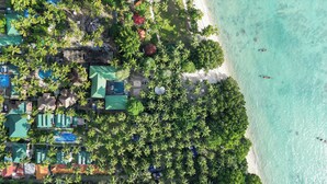 Luftaufnahme eines Resorts mit mehreren Gebäuden, einem Strand und klarem, türkisblauem Wasser.