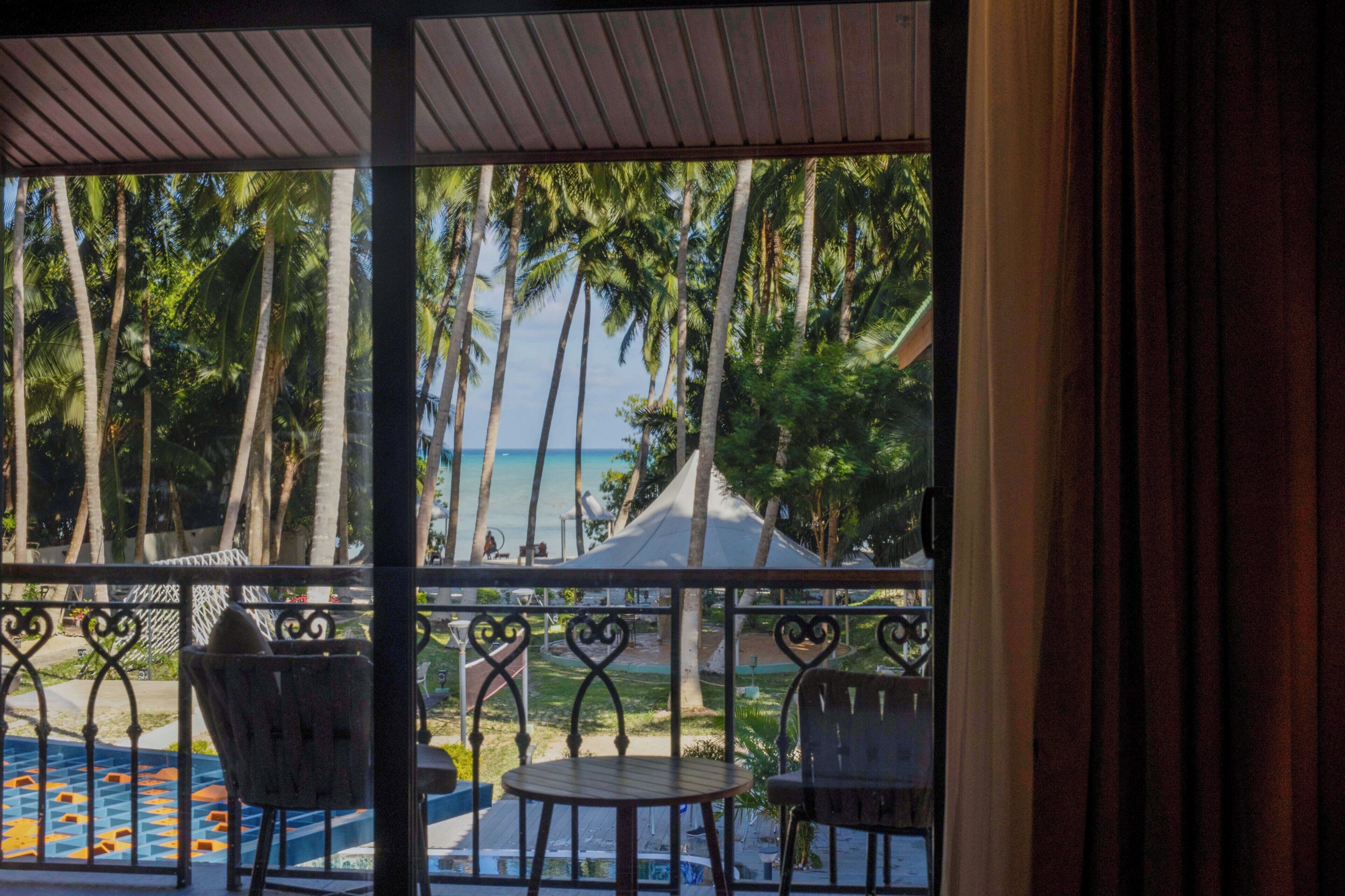 A balcony with a view of palm trees and the ocean.
