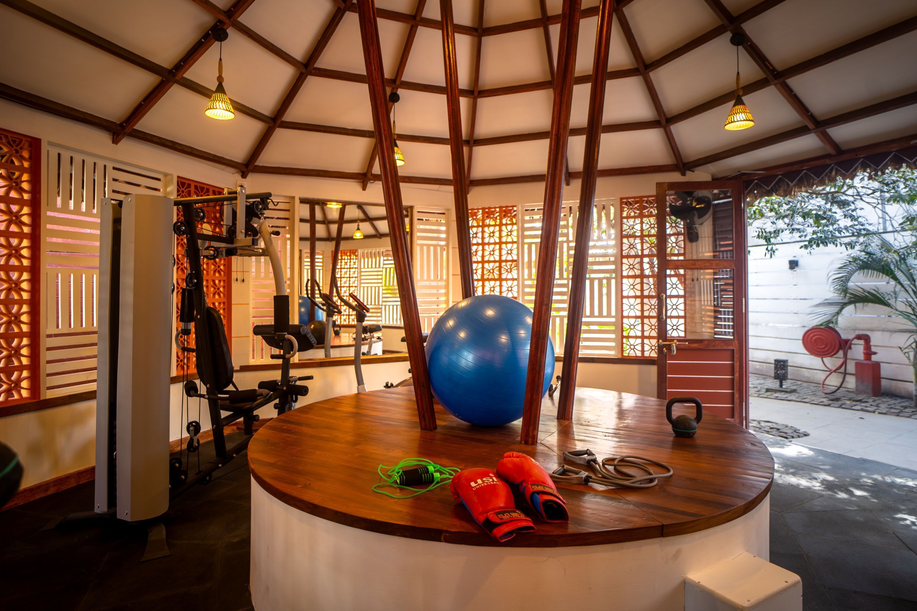 Een sportschool met trainingsapparatuur, een grote blauwe fitnessbal en een houten tafel met rode schoenen en een kettlebell.