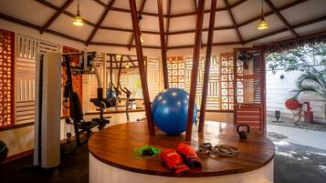 Een sportschool met trainingsapparatuur, een grote blauwe fitnessbal en een houten tafel met rode schoenen en een kettlebell.