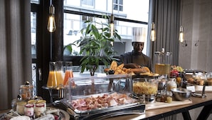 Un buffet proposant une variété de plats, un chef cuisinier et une grande fenêtre donnant sur des immeubles.
