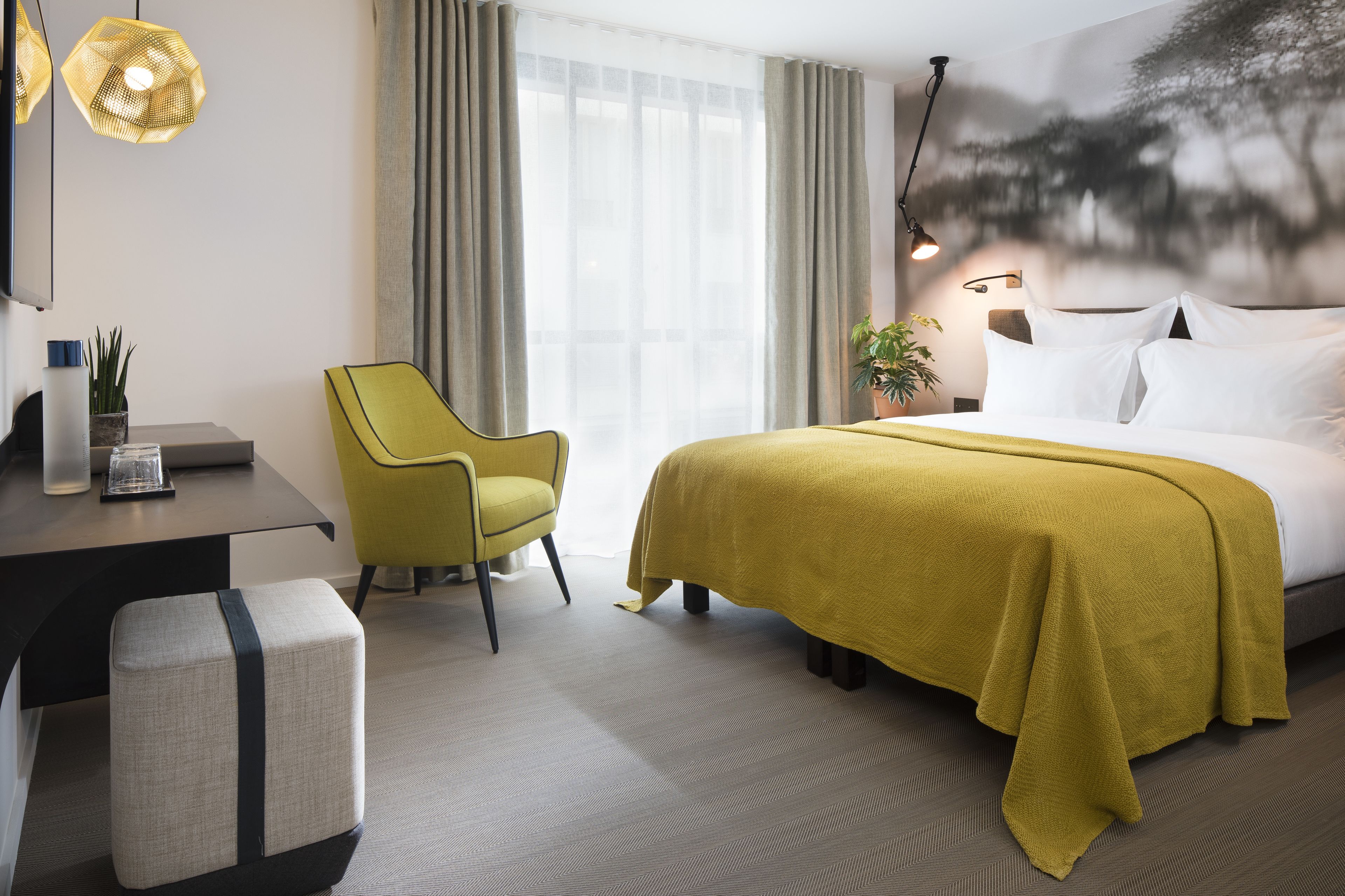Una habitación de hotel con cama, escritorio, silla y un ventanal con cortinas.