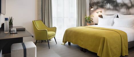 Una habitación de hotel con cama, escritorio, silla y un ventanal con cortinas.