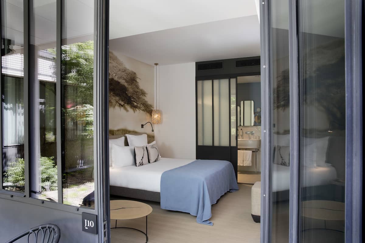 Una habitación de hotel moderna con cama, mesita de noche y vistas al exterior.