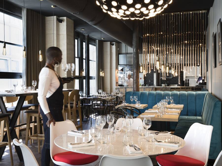 En restauranginteriör med bord som är dukade för middag, en bardisk och en sittgrupp.