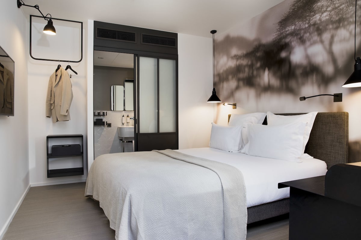 Una habitación de hotel moderna con una cama grande, un escritorio, un armario y un baño visible a través de una puerta abierta.