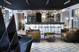 A modern bar area with a bar counter, stools, and a variety of bottles. There are sofas and a coffee table in the seating area.
