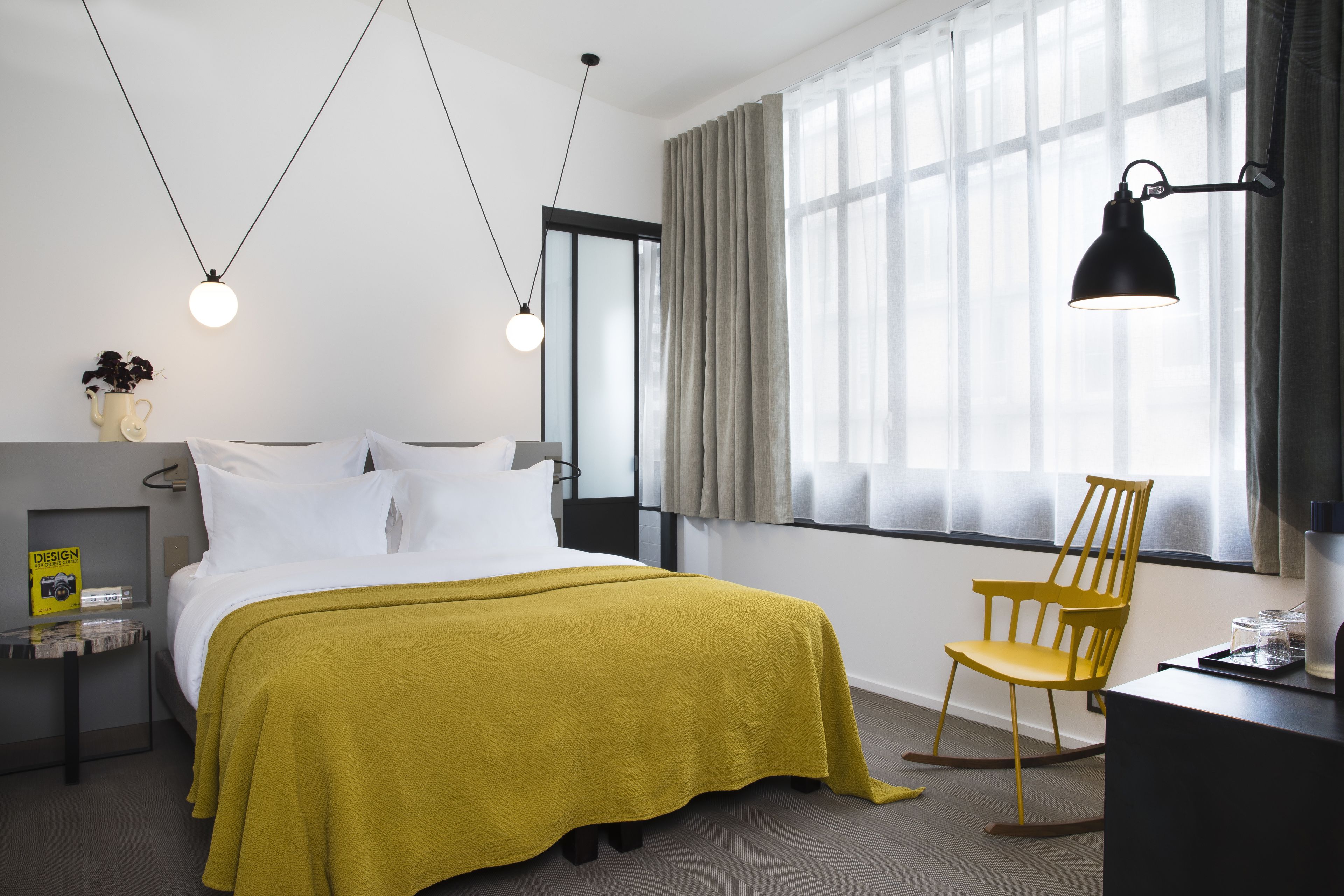 A modern hotel room with a bed, a desk, a chair, and a large window with curtains.