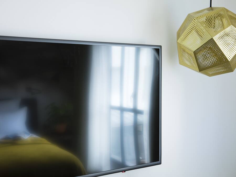 Ein Flachbildfernseher an der Wand, darüber eine geometrische Pendelleuchte.