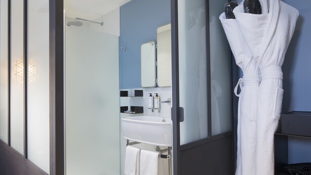 Une salle de bain moderne avec une douche à parois de verre, un lavabo blanc et un peignoir suspendu à un porte-serviettes.