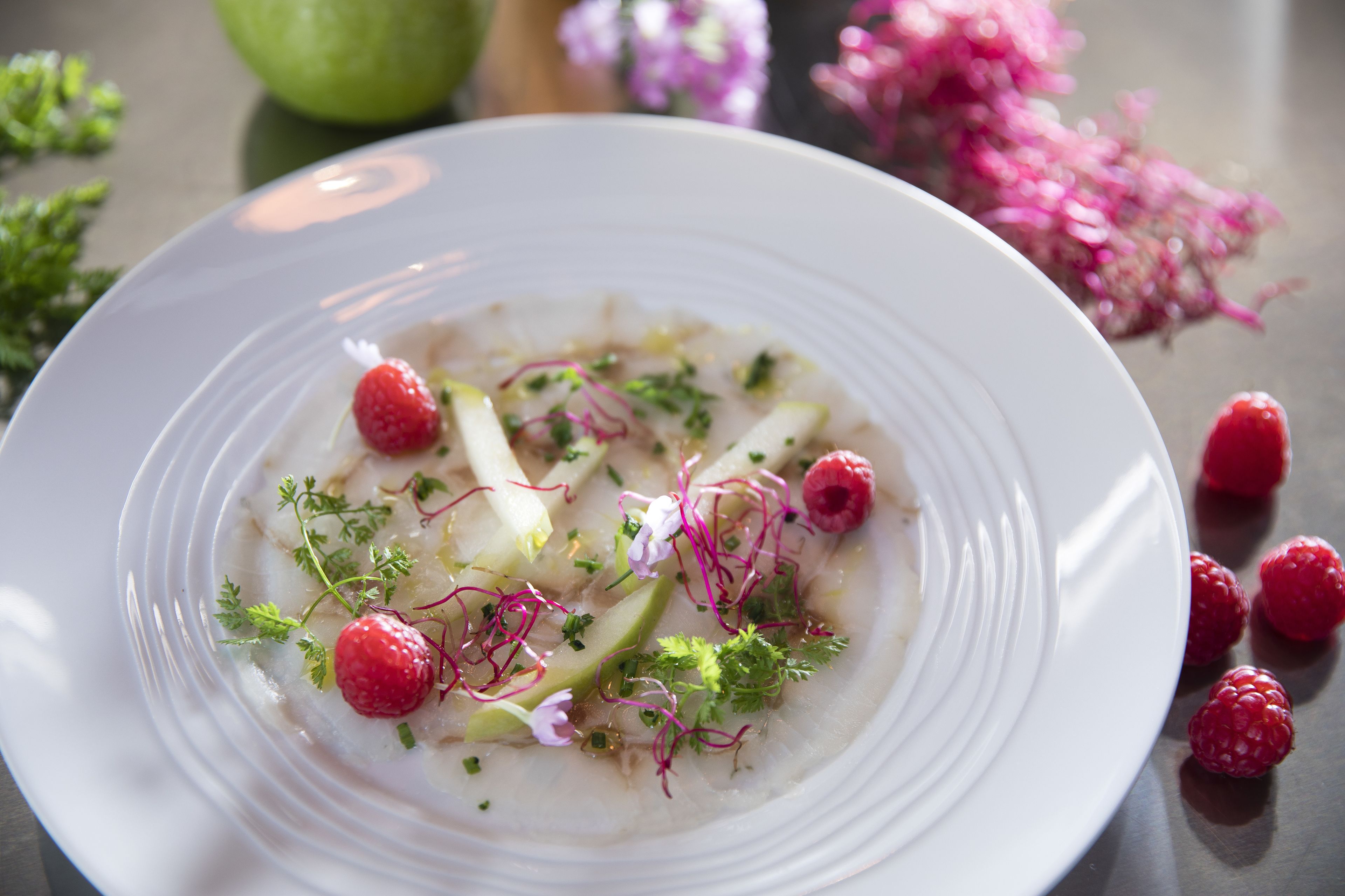 A white plate with a dish garnished with raspberries, herbs, and possibly some greens.