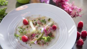 A white plate with a dish garnished with raspberries, herbs, and possibly some greens.