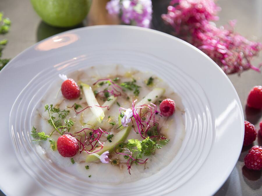 A white plate with a dish garnished with raspberries, herbs, and possibly some greens.