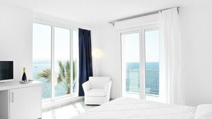A hotel room with a bed, a desk with a TV, a chair, and large windows with curtains.