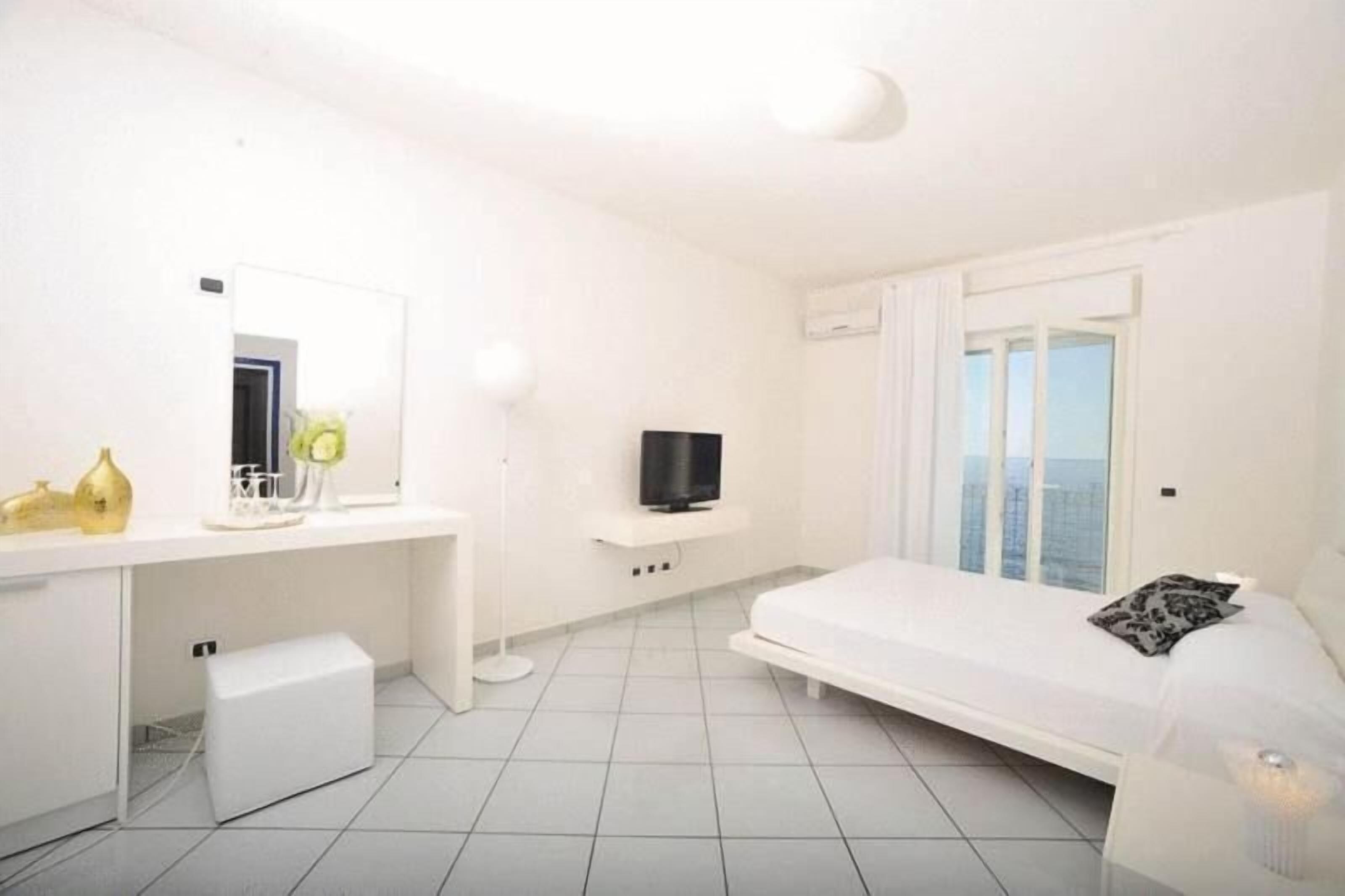 A modern hotel room with a bed, a TV, a desk with a mirror, and a window with curtains.