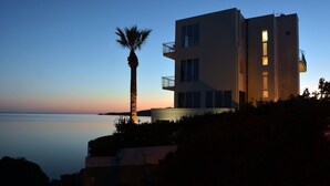 A modern building with balconies overlooking a calm body of water during twilight.