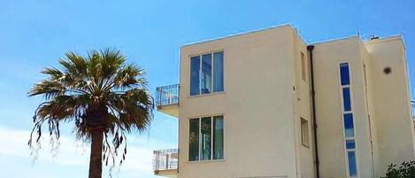 A modern two-story building with large windows and a balcony, located near a body of water.