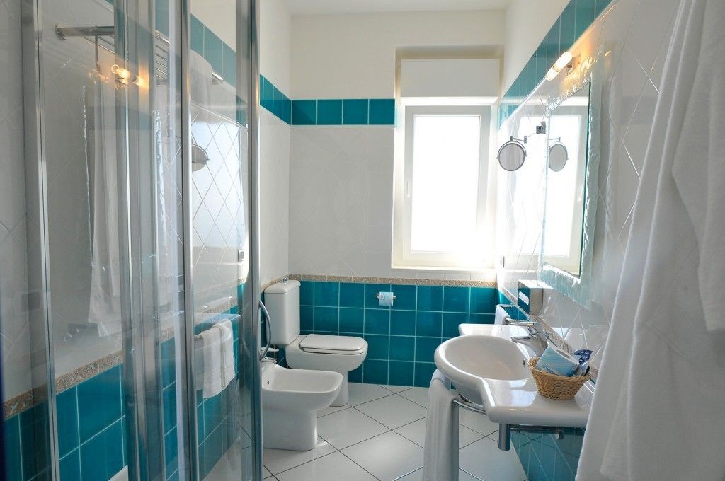 Une salle de bain dotée d’une douche à parois de verre, de toilettes, d’un bidet, d’un lavabo et d’une fenêtre laissant entrer la lumière naturelle.