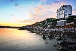 A coastal hotel with a modern design, featuring a stone facade and a balcony overlooking the sea. - Villa Grachira (Alghero)