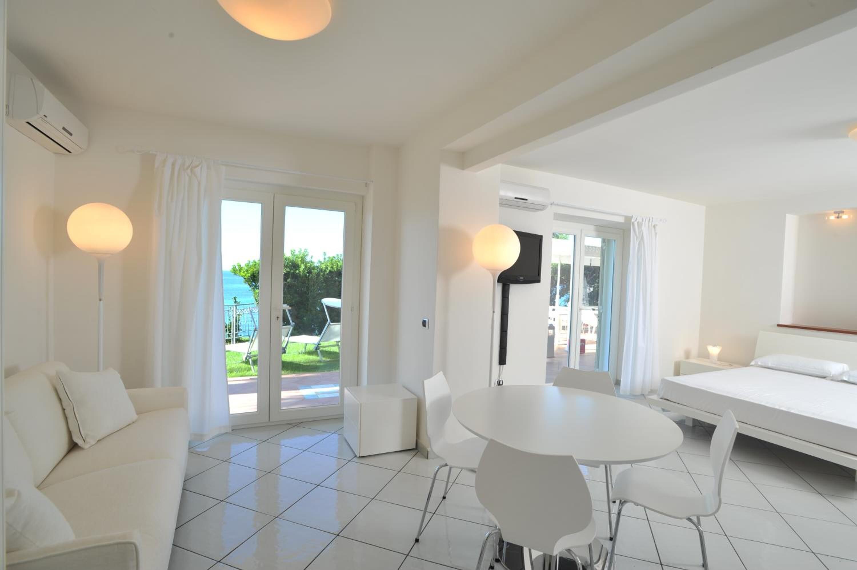 Une chambre d’hôtel moderne avec un canapé blanc, une table de salle à manger ronde et un lit.