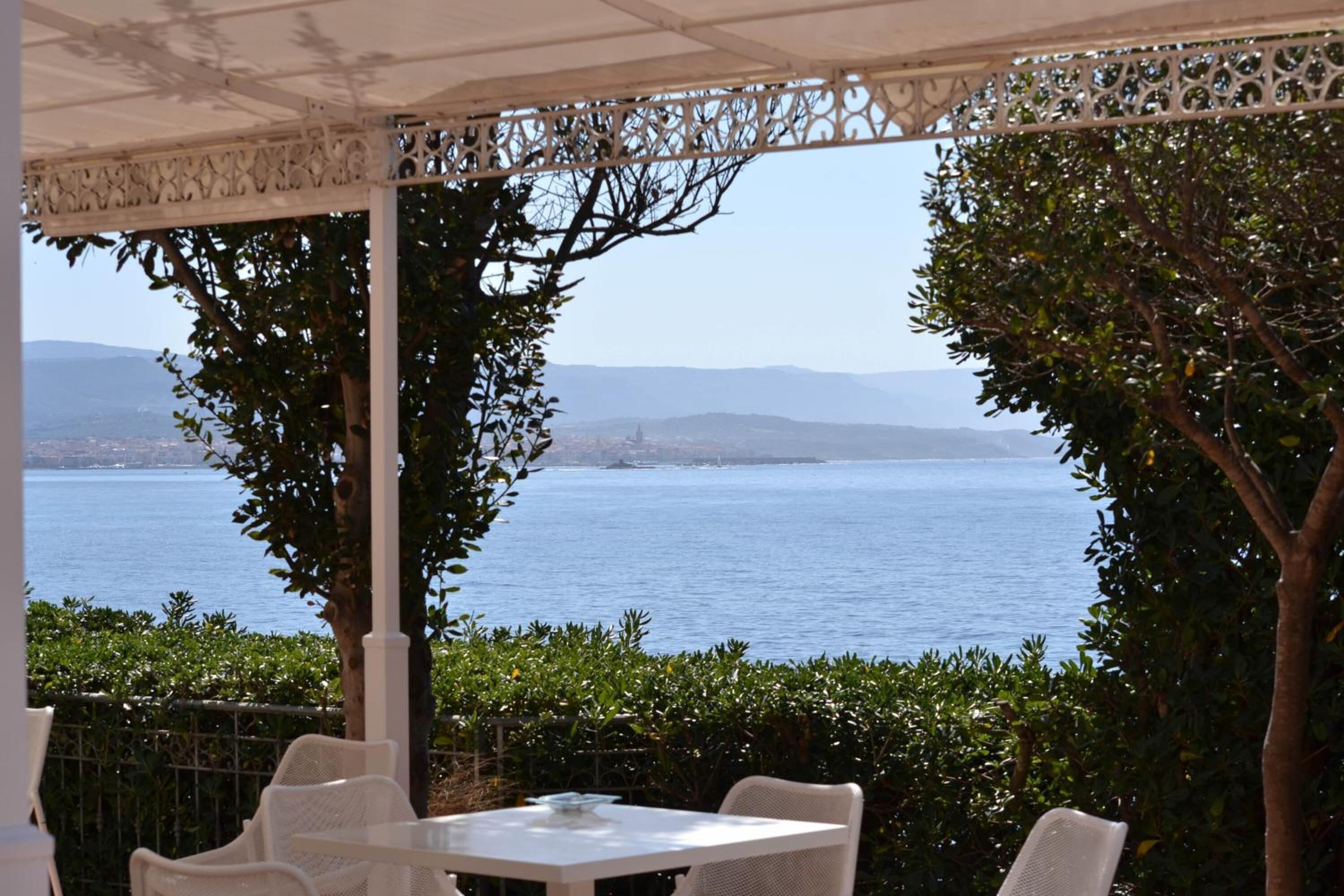 An outdoor seating area with white chairs and tables, overlooking a body of water and distant hills.