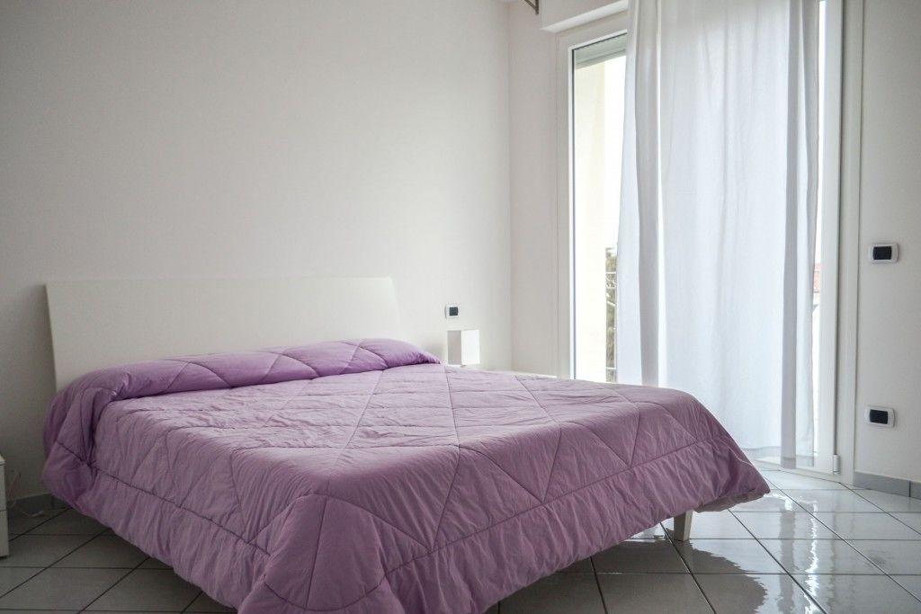 Een slaapkamer met een groot bed, een nachtkastje en een raam met gordijnen.