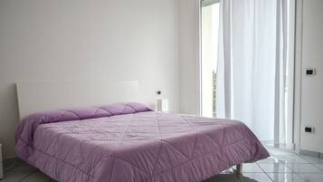 Een slaapkamer met een groot bed, een nachtkastje en een raam met gordijnen.