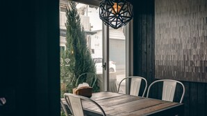 A dining area with a wooden table and white chairs, a hanging light fixture, and a view of a tree and buildings outside. - Original Hostel (Chishang)