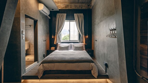 A bedroom with a large bed, a window with curtains, a wooden ceiling, and a view of the city. - Original Hostel (Chishang)