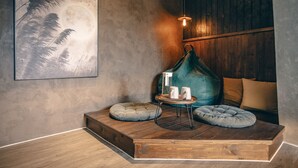 A cozy room with a wooden platform, two round cushions, a small table with cups, and a wall-mounted lamp. - Original Hostel (Chishang)