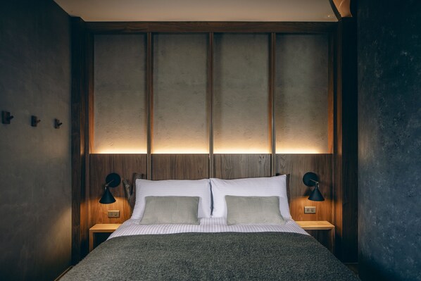 A neatly made bed with a wooden headboard, two bedside lamps, and a textured wall. - Original Hostel (Chishang)