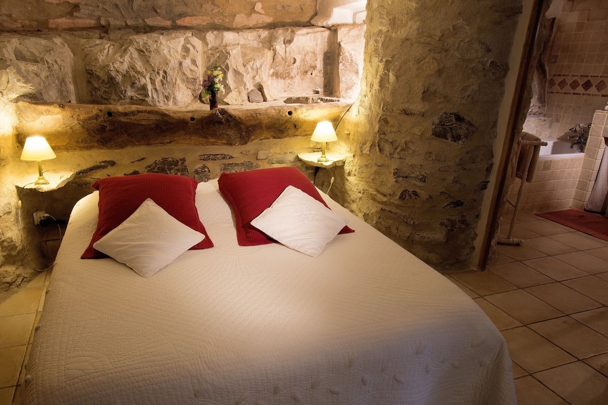 Une chambre aux murs de pierre, avec un lit, deux lampes de chevet et une petite fenêtre.
