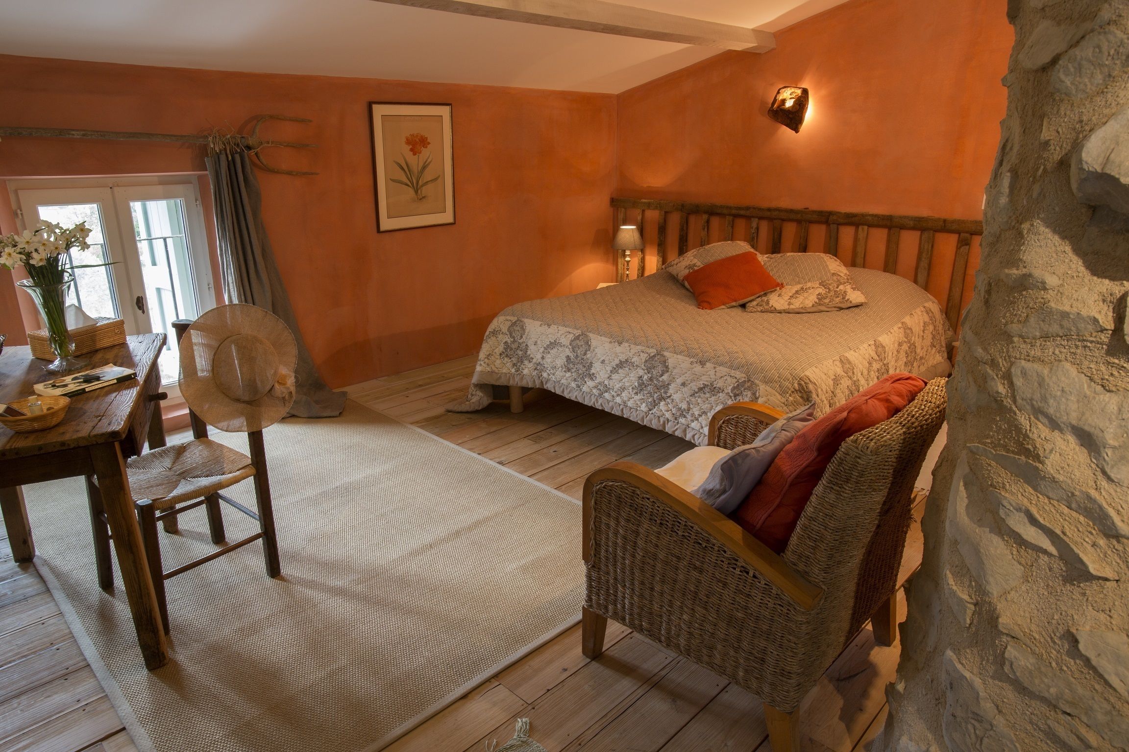 A cozy bedroom with a bed, a chair, a table, and a stone wall.
