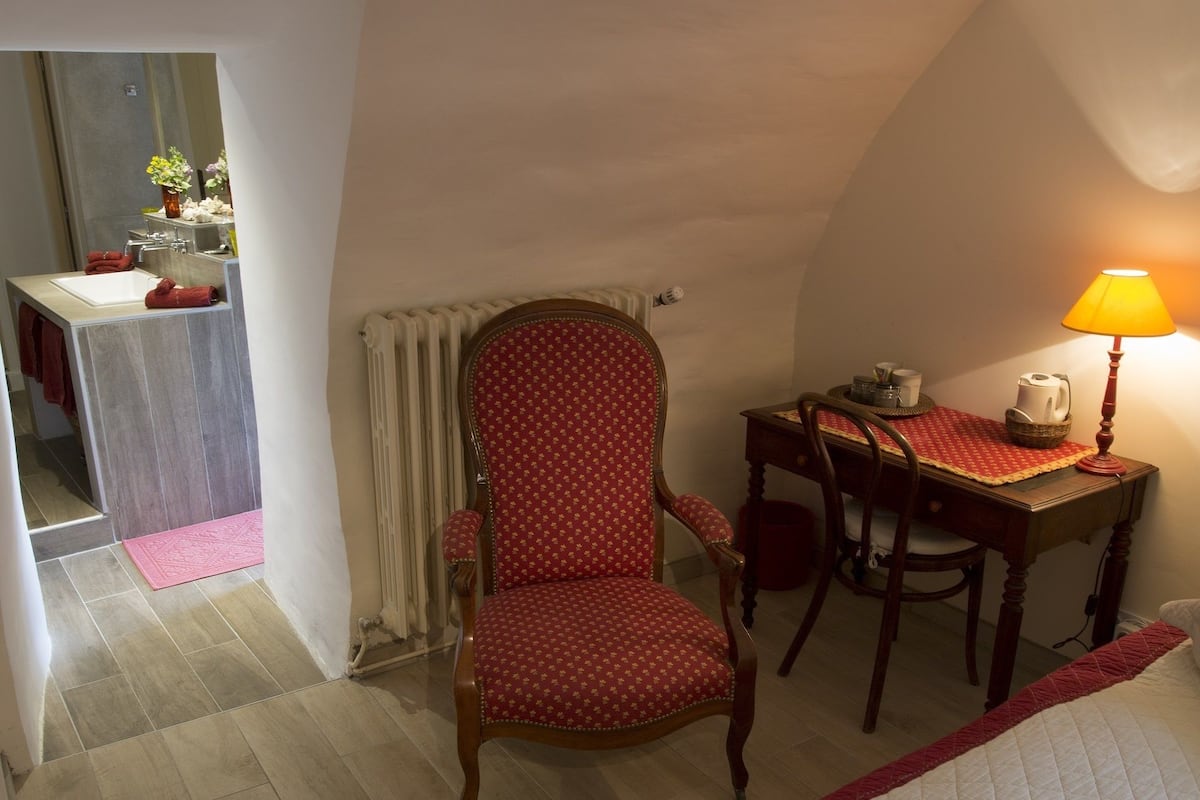 Une chambre à coucher comprenant un lit, une chaise, une table avec une lampe et donnant sur une salle de bain.